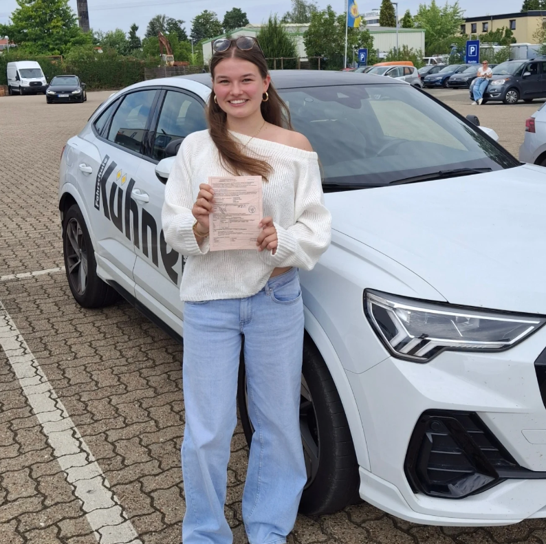 Fahrschülerin mit bestandener Prüfung vor dem Ausbildungsfahrzeug